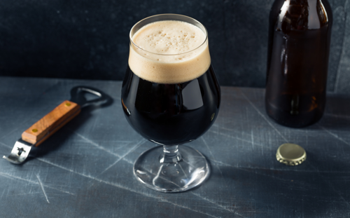 A glass of stout, bottle opener, bottle and removed cap
