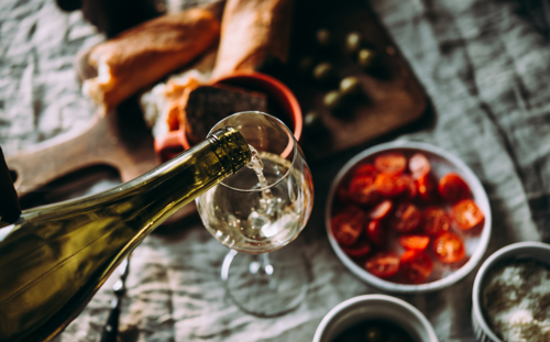 White wine being poured into a glass with food in the background