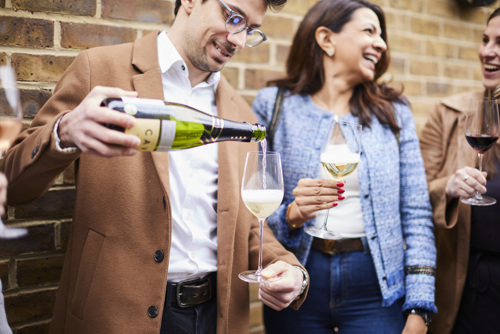 Man pouring wine, surrounded by a group of people holding wine glasses